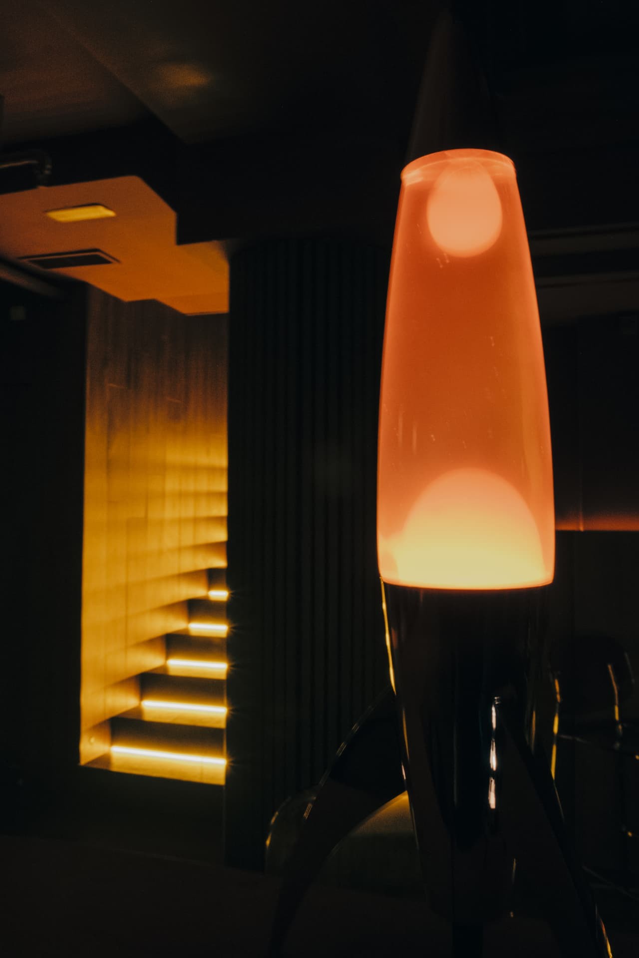 Escalera iluminada que baja a Baja Frecuencia, junto a una lámpara de lava